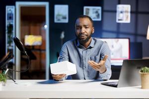 BIPOC tech content creator filming technology review of newly launched smartphone, unboxing it and presenting specifications to audience. Influencer showing mobile phone to viewers photo