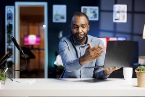 African American man assessing laptop, expressing dissatisfaction with subpar components quality. Content creator shooting for online channel, displeased with notebook device performance photo