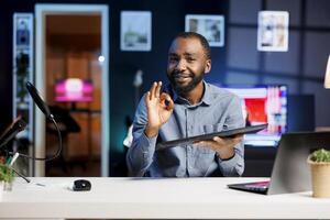 Content creator presenting gaming keyboard to subscribers, giving guarantees about precision and power. Tech expert showing ok hand sign, happy about computer peripheral after testing it photo