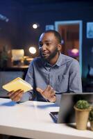 Influencer in studio using camera to capture live broadcast, reviewing new book from publisher. BIPOC online show host filming literature critique, presenting new novel from esteemed author to viewers photo