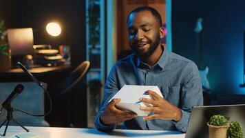 BIPOC tech content creator filming technology review of newly released smartphone, unboxing it and presenting parameters to audience. Internet star showing phone to subscribers photo