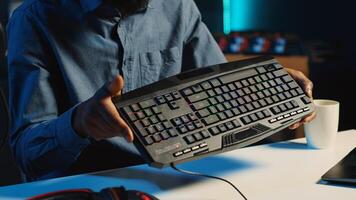 African american content creator in dimly lit living room uses camera to film RGB lights keyboard review for online streaming platforms. Media star hosts internet show, unboxing peripherals, close up photo