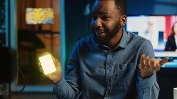 BIPOC tech content creator filming technology review of mini RGB lights device illuminating in different colors. Internet star showing helpful production tool to subscribers photo