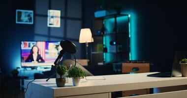 Empty home studio interior illuminated with neon lights at night, used for internet show production. Apartment filled with content creation equipment, TV running in background, handheld camera shot photo