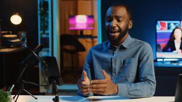 Content creator in dimly lit home studio using cellphone camera to film for online streaming platforms. Influencer greets audience using mobile phone to record footage photo