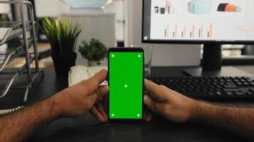POV of manager holds smartphone with isolated greenscreen layout, working with blank mockup chromakey template at office desk. Young man looking at mobile device display with copyspace. photo