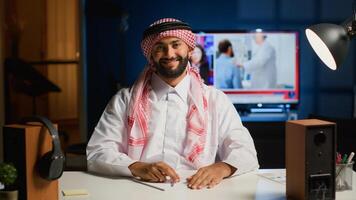 Portrait of smiling arab man engaged in elearning class conference communication. Muslim student in online videocall greeting tutor, listening to his teachings while taking notes photo