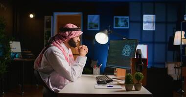 Licensed arabic engineer updating neural networks, writing intricate binary code scripts on computer. Middle Eastern man uses digital device programming to upgrade AI datasets at home photo