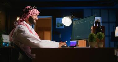 Smiling muslim engineer writing script code on computer screen using Java programming languages. Self employed Middle Eastern developer at home working on fixing database errors photo