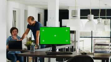 Workstation displaying greenscreen layout with copyspace on monitor at empty desk in urban coworking space. Chromakey display equipment adopted in smaller company operations. Tripod shot. photo