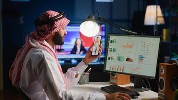 Muslim teleworker and coworkers in call crosschecking analytics statistical data sets in dimly lit apartment office. Arab employee optimizing key performance indicators with colleagues in videocall photo