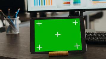 Digital tablet presenting greenscreen display on agency office desk, showing blank chromakey template at empty workstation. Modern mobile device displaying isolated chromakey concept. Close up. photo
