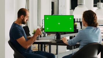 Corporate team using greenscreen on monitor while sitting at agency workstation, small business development. Man and woman colleagues looking at display showing isolated copyspace. photo