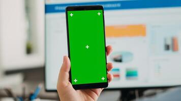 Company worker holding smartphone with greenscreen template, using digital chromakey template on mobile gadget display. Employee presenting isolated mockup copyspace in business office. photo