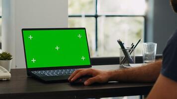 Male employee looks at greenscreen chromakey display while he sits at creative agency workstation, working on e commerce operations. Professional analyst checks blank mockup layout on laptop. photo