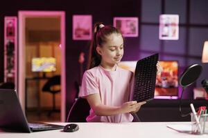Small girl showing subscribers mechanical keyboard received from sponsoring brand to promote it. Kid in pink studio advertising wireless gaming computer peripheral from partnering company photo