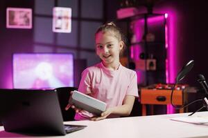 Child media star filming about best Bluetooth music playing devices of the year. Cute girl tech content creator recording portable speaker review, assessing audio quality photo