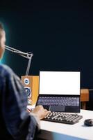 Black woman working from home at a desk with wireless computer displaying an isolated white screen. African american person using digital laptop showing blank chromakey mockup template. photo