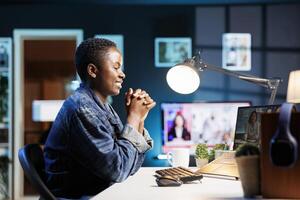 African american freelancer with laptop is attending an online meeting in a living room. Smiling black woman engages in virtual communication from home, using technology for remote work. photo