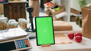Greenscreen on tablet at checkout desk in local organic shop with freshly harvested produce, vendor using isolated chromakey template on gadget. Shop owner shows blank mockup display. photo