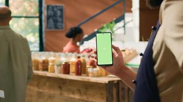 Local seller holds smartphone app with greenscreen display, presenting copyspace technology on mobile device. Young man showing isolated mockup screen at grocery store checkout. photo