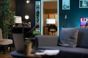 Stylish empty apartment with artwork on walls and computer screen left open at night showing software interface. Home living room with no people in, cozy couch and TV left open photo