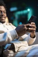 Focus on cellphone used by man in blurry background to compose messages, chatting with internet friends. Close up of mobile phone used by person to scroll on social media feed while in apartment photo
