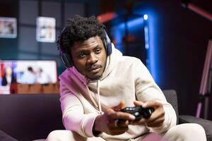 Gamer relaxing at home, sitting down on couch, excited to play games and enjoy leisure time. Man sitting on couch in apartment, playing videogame on gaming console, relaxing after work photo