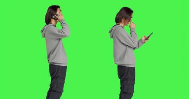 Young man answering call and texting in studio with greenscreen backdrop, talking remotely on smartphone and messaging. Asian male model using mobile phone for different actions. photo