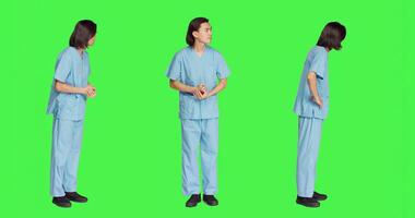 Over greenscreen wall, healthcare worker awaits for event, dressed in hospital protective outfit and being anxious. Man with medical expertise and natural abilities stands in studio. photo