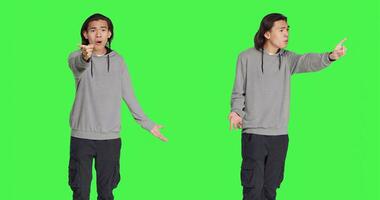 Young man showing no gesture in studio, expressing negativity and disagreement over isolated greenscreen backdrop. Asian male model being disappointed and disapproving with something. photo