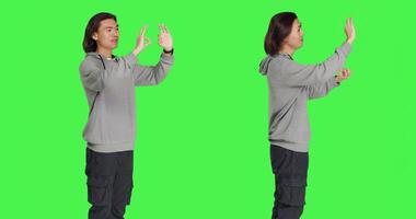Young model showing okay symbol in studio, acting pleased and happy with something over greenscreen backdrop. Asian man feeling positive and shows agreement or gives his approval. photo
