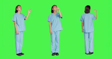 asiático médico enfermero cheques holograma en estudio con pantalla verde diseño, trabajando con holográfico icono lengüeta y artificial inteligencia. masculino especialista en uniforme con cuidado de la salud pericia. foto