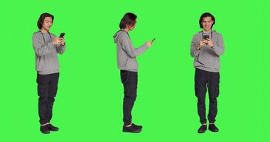 Adult texting messages on phone standing over greenscreen background, using social media app to chat remotely with friends. Asian joyful person messaging on modern smartphone. photo