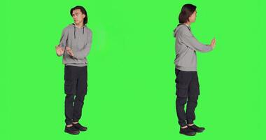 Person pretending to push thing aside, expressing rejection or denial in studio. Young adult mimicking refusal over isolated full body greenscreen background, stop symbol on camera. photo