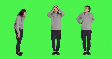 Male person suffering from back ache in studio, dealing with lower spine cramps while he is standing over full body greenscreen. Young man being in pain and suffering from spinal pain. photo