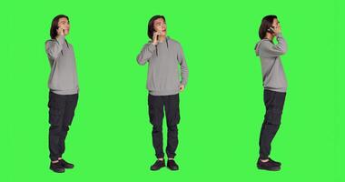 Modern guy talking on smartphone call over full body greenscreen, using telephone line to talk to his colleagues in studio. Young person answering call to have remote discussion. photo