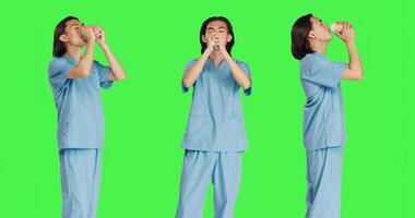 Asian specialist enjoying coffee cup against greenscreen backdrop, male nurse with healthcare expertise drinking hot caffeine refreshment in studio. Medical assistant with uniform. photo