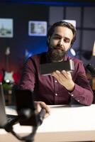 Media star doing technology review of wireless portable speaker for, filming with phone on selfie stick. Influencer showcasing music playing device, capturing footage with cellphone camera photo