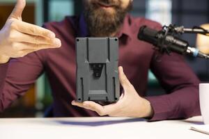 Close up shot of portable V mount battery presented by knowledgeable expert to audience. Focus on lithium li-ion charging device held by content creator in blurry background photo