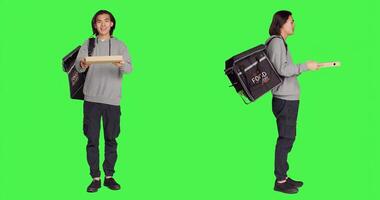 Asian man delivering food for clients using thermal bag over full body greenscreen, carrying meal orders. Deliveryman employee posing on camera, providing takeaway aliments. photo