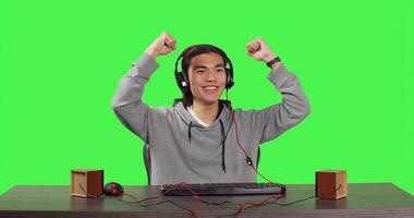 POV of asian adult enjoying computer games at desk while sitting over full body greenscreen backdrop. Gamer has fun with friends online in gaming web challenge, using headphones at desktop. photo