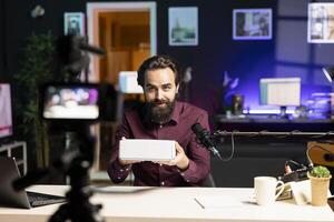 Tech guru filming packaged product unboxing for technology vlog using professional camera. Influencer urging fans to buy sponsoring partner merchandise, recording with high quality gear photo