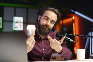 Tech guru teaching viewers how to do maintenance on smart light bulb. Content creator hosting technology show, doing tutorial on how to fix broken IoT home automation product photo