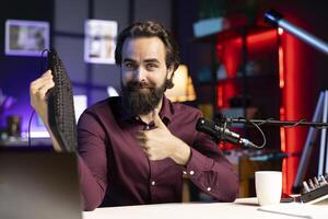 Influencer in studio reviewing gaming keyboard received from sponsoring brand. Online show host paid to promote bluetooth wireless computer peripheral to viewers during live broadcast photo