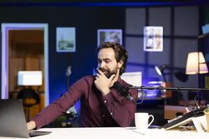 Man reading from laptop in studio, looking perplexed at recent news headlines, sharing opinions with audience. Show host talking with subscribers, feeling shocked by information he found online photo