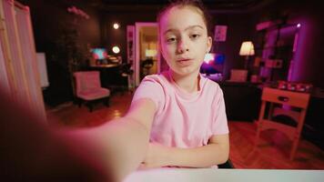 Kid films POV style with smartphone in pink neon lit living room used as professional studio. Young online star captures footage with selfie cellphone camera, discussing about fun day at school photo