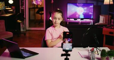 Zoom in shot of kid talking about school with children audience, filming content for social media with cellphone attached to tripod. Young girl recording for internet channel with mobile phone photo