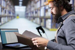 Industrial worker reading shipment invoice details in warehouse, supervising dispatch notes and order receipts in folder. Facility engineer working on supply chain management and quality control. photo