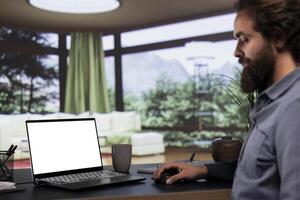 Young billionaire looks at white display layout on laptop, getting cozy in his extravagant alpine villa. Influential entrepreneur uses computer to check blank copyspace screen on pc, teleworking. photo